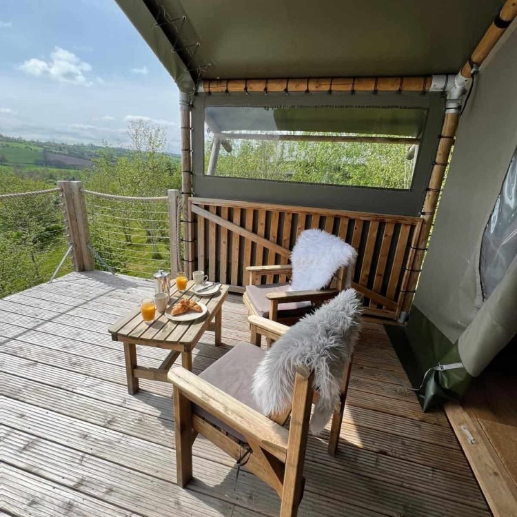 Private deck at Oaklands safari tent with wooden chairs, sheepskin throws and breakfast overlooking the Mid Wales countryside.