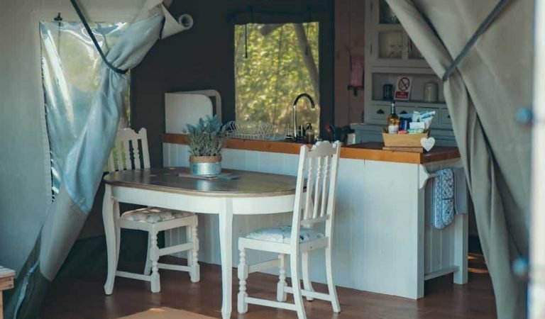Cosy rustic kitchen and dining area inside the Oaklands safari tent, featuring a white wooden table and countryside-inspired décor.