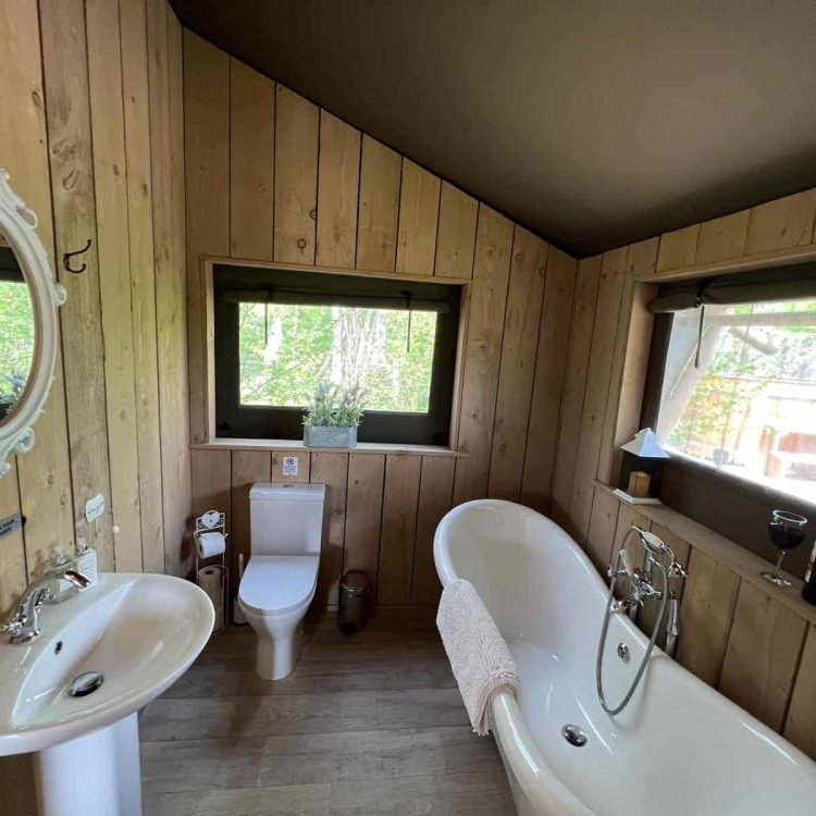 Luxury safari tent bathroom with freestanding roll-top bath and woodland views at Oaklands Glamping Wales.
