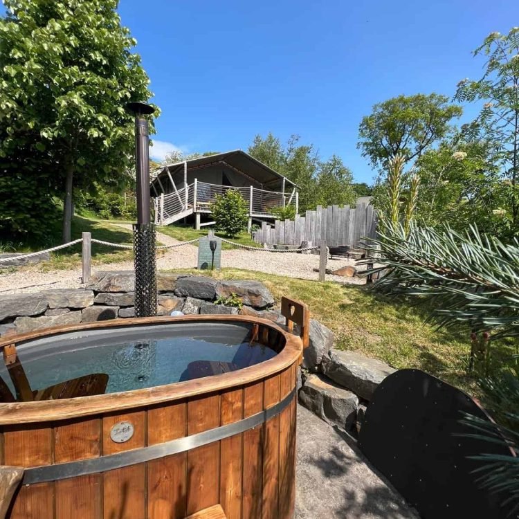 Wood-fired hot tub outside the safari tent with clear blue skies and scenic rural views.