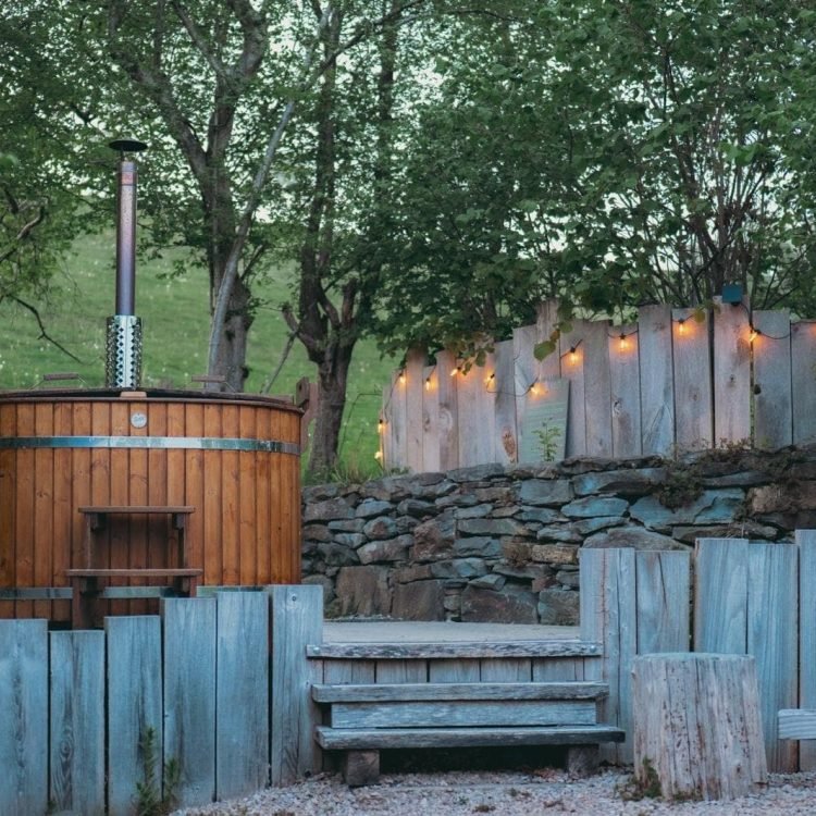 Wood-fired hot tub in a rustic outdoor area with soft evening lighting and natural stone landscaping at Oaklands Safari Tent.