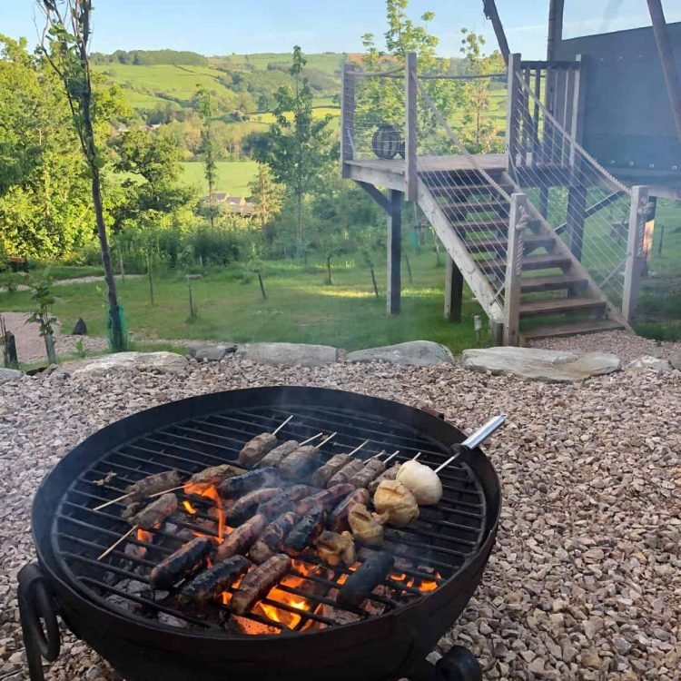 Outdoor fire pit barbecue cooking skewers with panoramic countryside views beside the Oaklands safari tent.