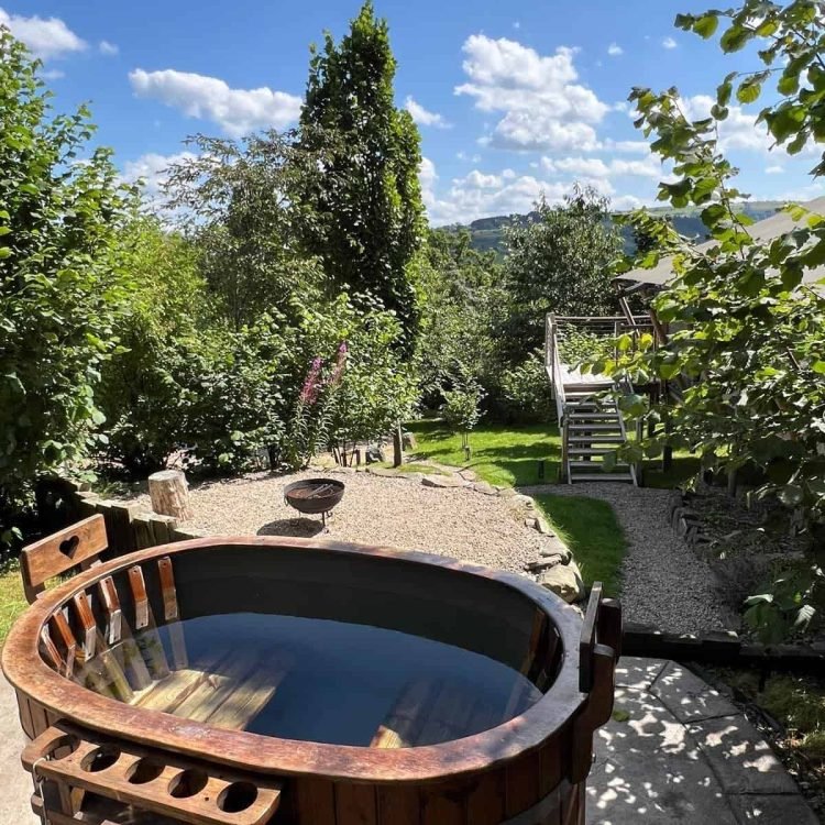 Wood-fired hot tub surrounded by greenery with countryside views at Oaklands Glamping, Mid Wales.