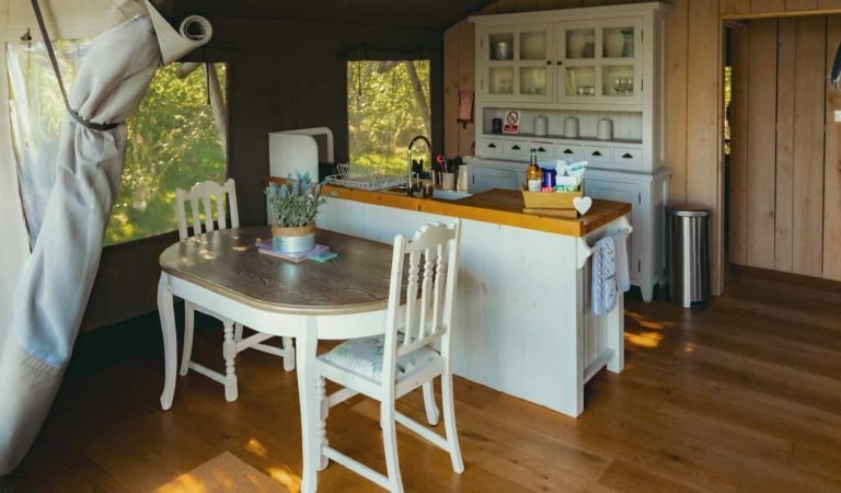 Dining table and kitchen area in the Oaklands safari tent, showcasing country-chic furniture and natural wood finishes.