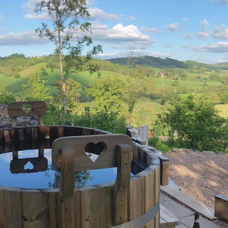 a hot tub with a view of a fire pit area and welsh countryside