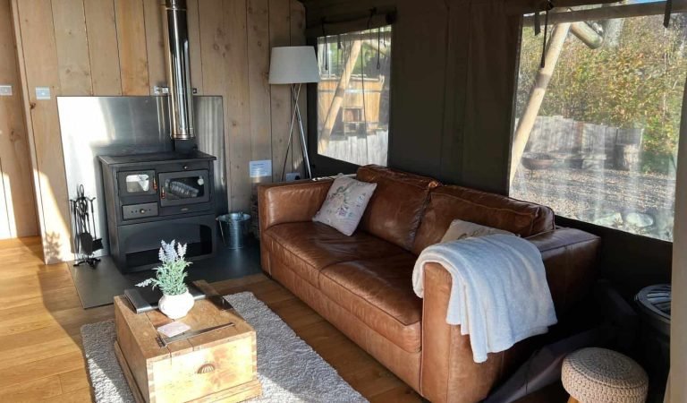 Cosy living room inside the Oaklands safari tent with a leather sofa, log burner and rustic wooden interior.