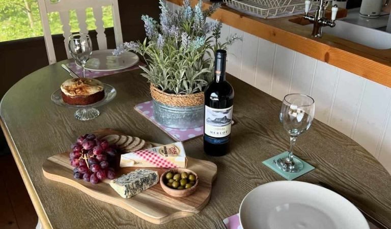 Rustic dining table inside the glamping lodge set with wine, cheese board and fresh flowers overlooking woodland views.