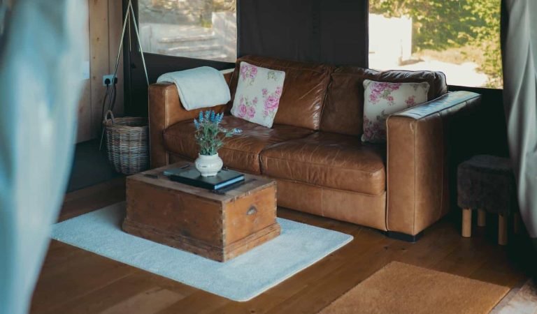 Cosy glamping lodge living area with a soft tan leather sofa, floral cushions and wooden coffee chest.