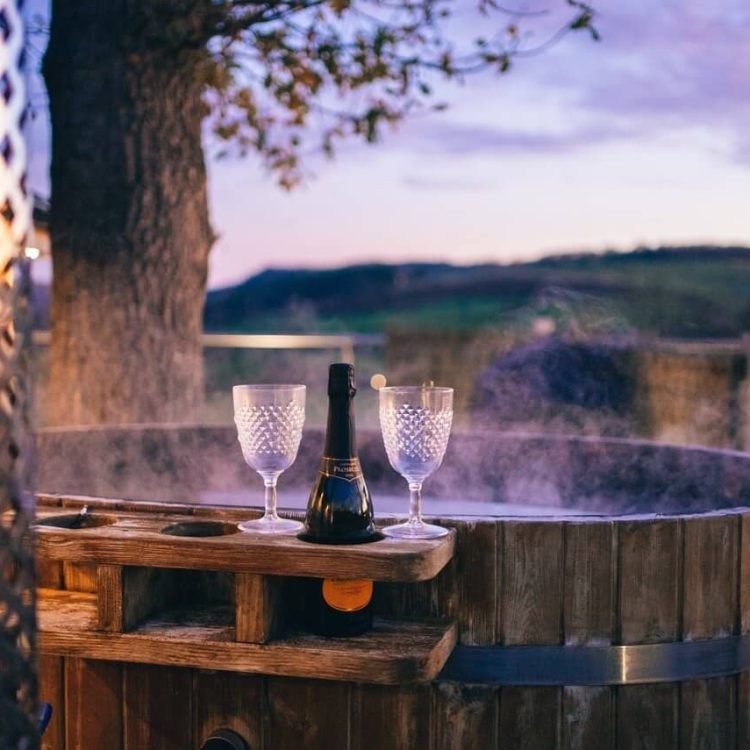 a steaming wooden hot tub with a bottle of wine and a glass