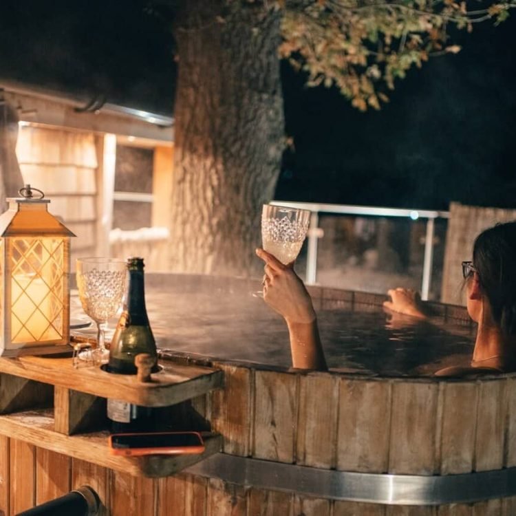 a woman soaking in a hot tub holding a glass of wine looking at the stars
