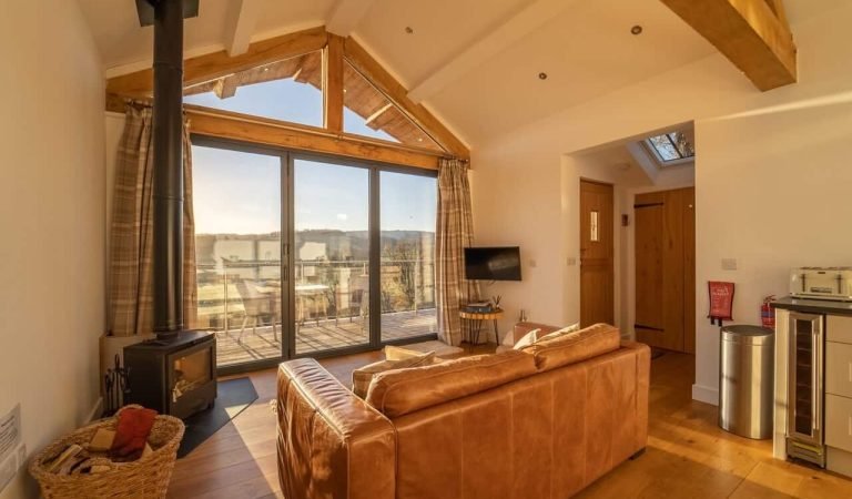 a large glass fronted living room that leads to decking lit by a sunrise