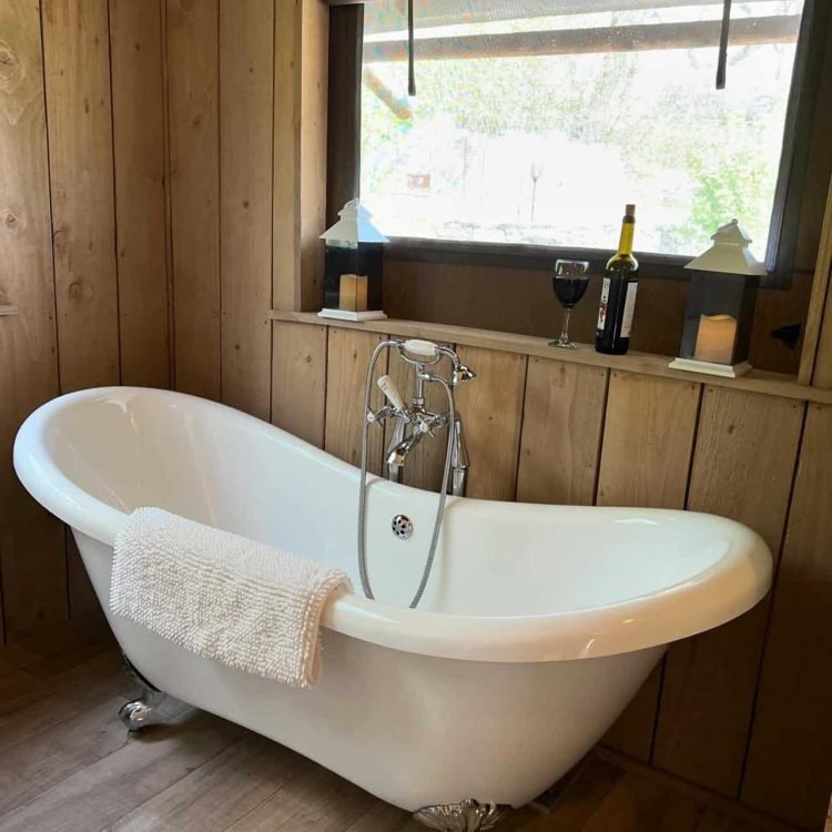 Roll-top bathtub positioned beside the window in the safari tent bathroom overlooking nature.