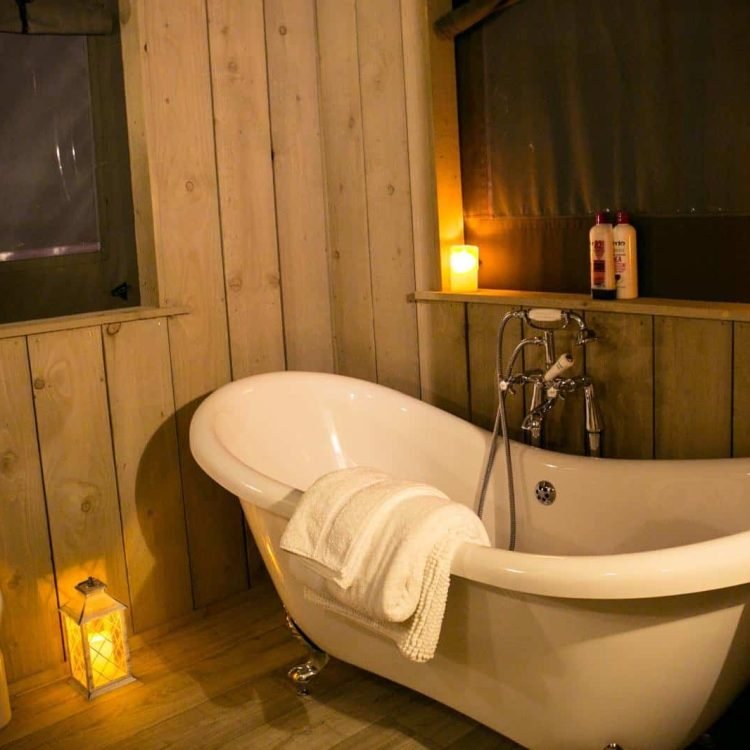 Cosy evening bathroom scene inside the safari tent with candles glowing around a luxury freestanding bath.